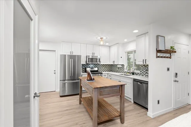 a kitchen with stainless steel appliances granite countertop a refrigerator a stove a sink and white cabinets with wooden floors