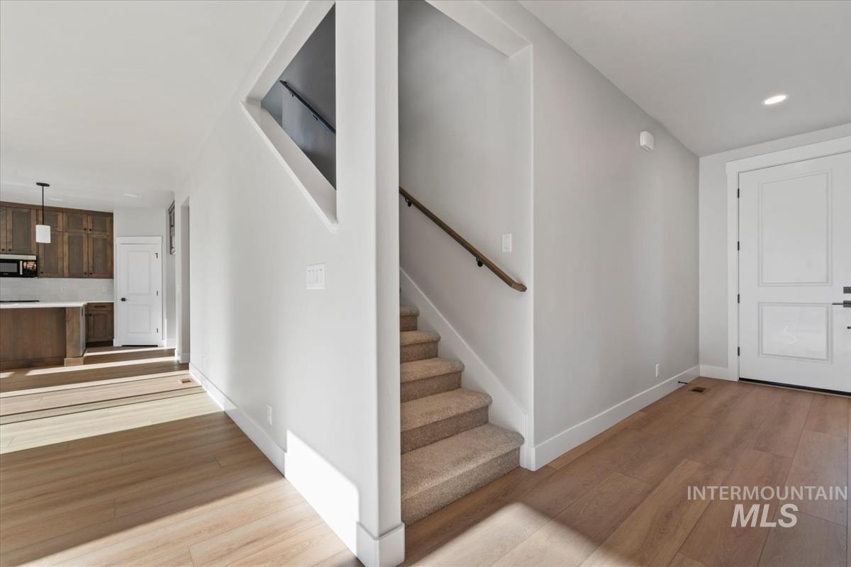 4223 Tropic Way Caldwell, ID 83607 - Photo 19 of 42 Entryway featuring light wood-finish flooring, a carpeted staircase with a wood handrail, a white paneled entry door, and recessed lighting