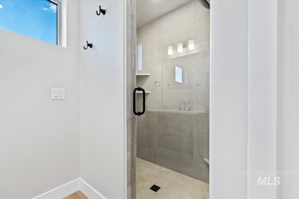 4223 Tropic Way Caldwell, ID 83607 - Photo 24 of 42 Walk-in shower featuring a glass enclosure with matte black hardware, tiled walls, built-in shelving, and a mosaic tile floor