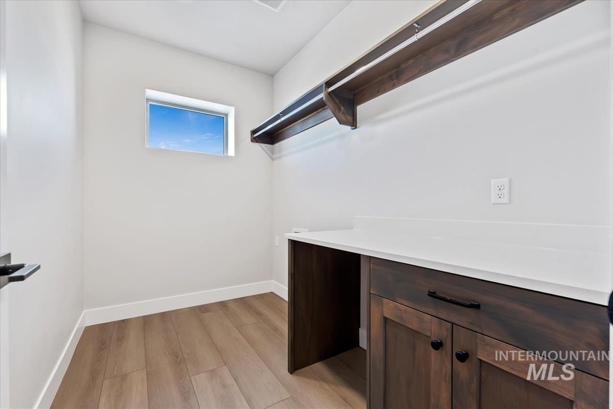 4223 Tropic Way Caldwell, ID 83607 - Photo 34 of 42 Utility room featuring wood-finish flooring, a wood-finish storage shelf, a built-in wood-finish cabinet with black hardware, and a white countertop