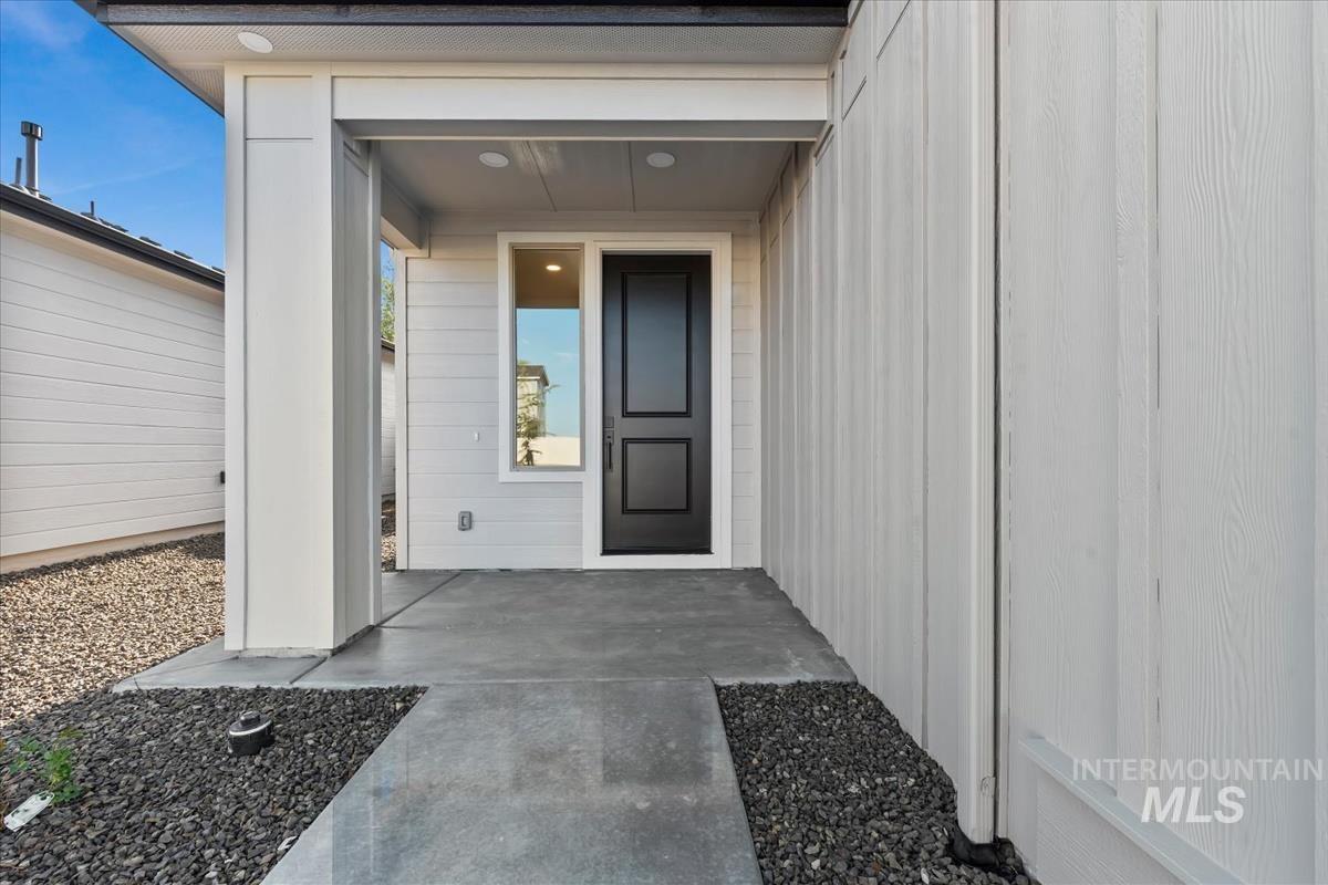4223 Tropic Way Caldwell, ID 83607 - Photo 40 of 42 Modern entryway featuring a black paneled door, horizontal siding, vertical board and batten siding, recessed lighting, and a concrete pathway with dark rock landscaping