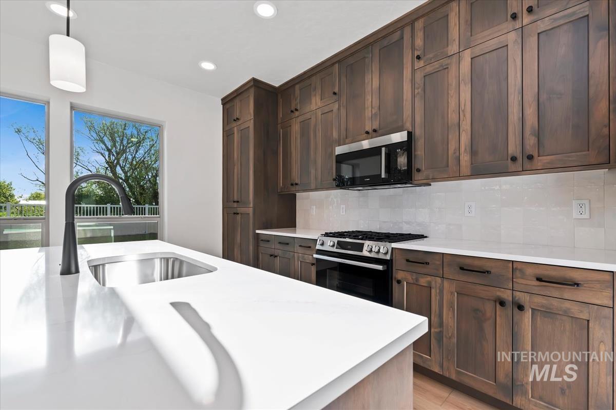 4223 Tropic Way Caldwell, ID 83607 - Photo 8 of 42 Kitchen featuring a large island with an undermount sink and matte black faucet, white countertops, wood-finish cabinetry, stainless steel appliances, and a tiled backsplash