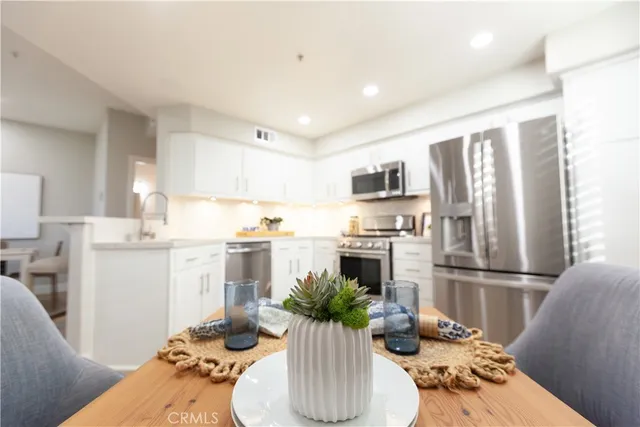 a kitchen with stainless steel appliances kitchen island granite countertop a refrigerator a stove top oven and a dining table with wooden floor