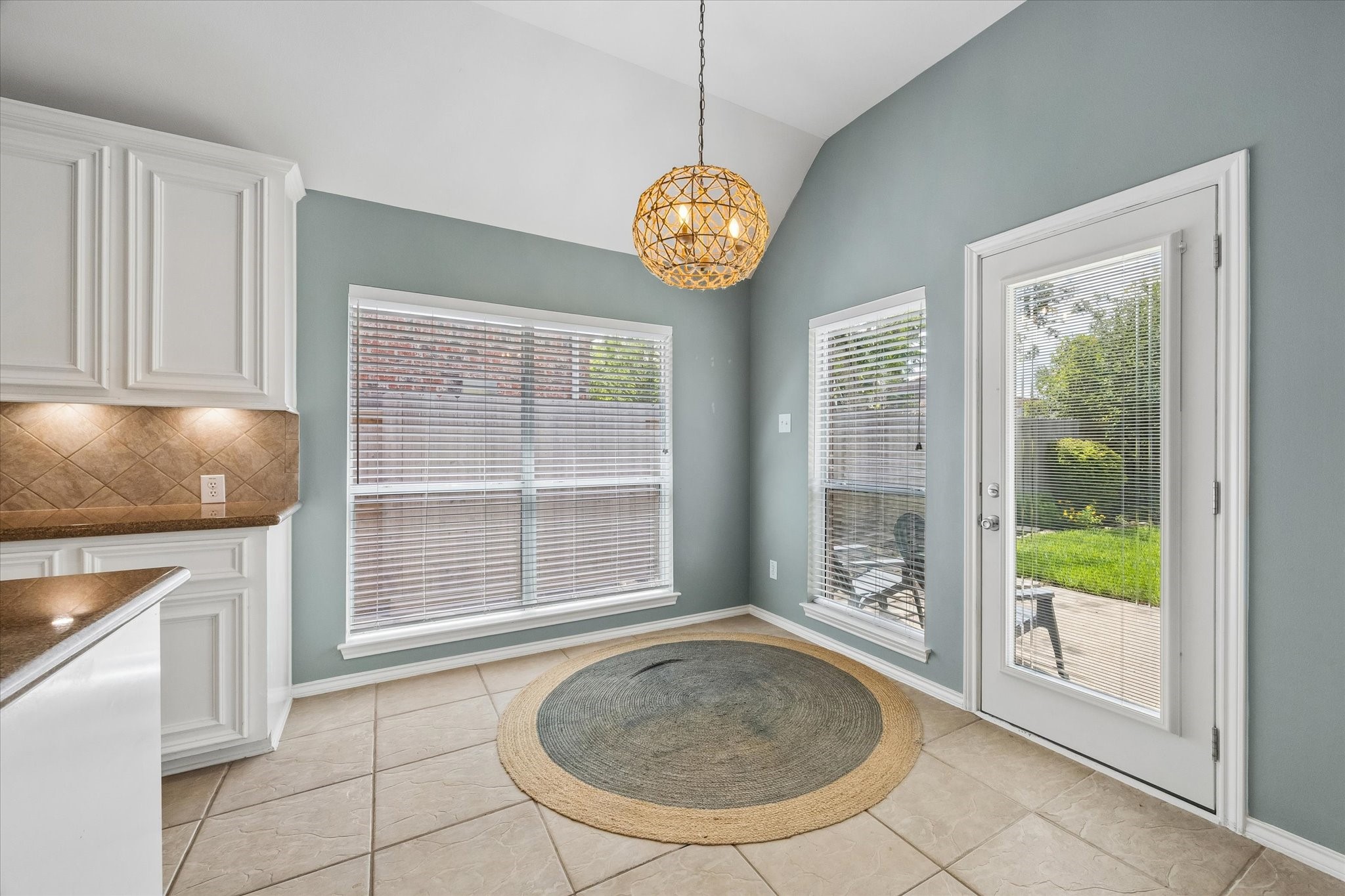 3118 Valley Court Manvel, TX 77578 - Photo 30 of 38 Bright dining area with large windows and patio door leading to a backyard. Features light blue walls, tiled flooring, white cabinetry, and a stylish hanging light fixture.