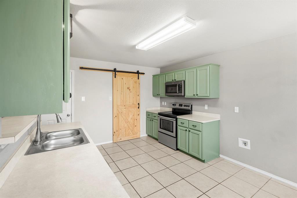 10620 Granada Drive Waco, TX 76708 - Photo 10 of 38 Kitchen featuring light green cabinetry, stainless steel appliances, a double basin sink, light-toned countertops, and a wood sliding barn door