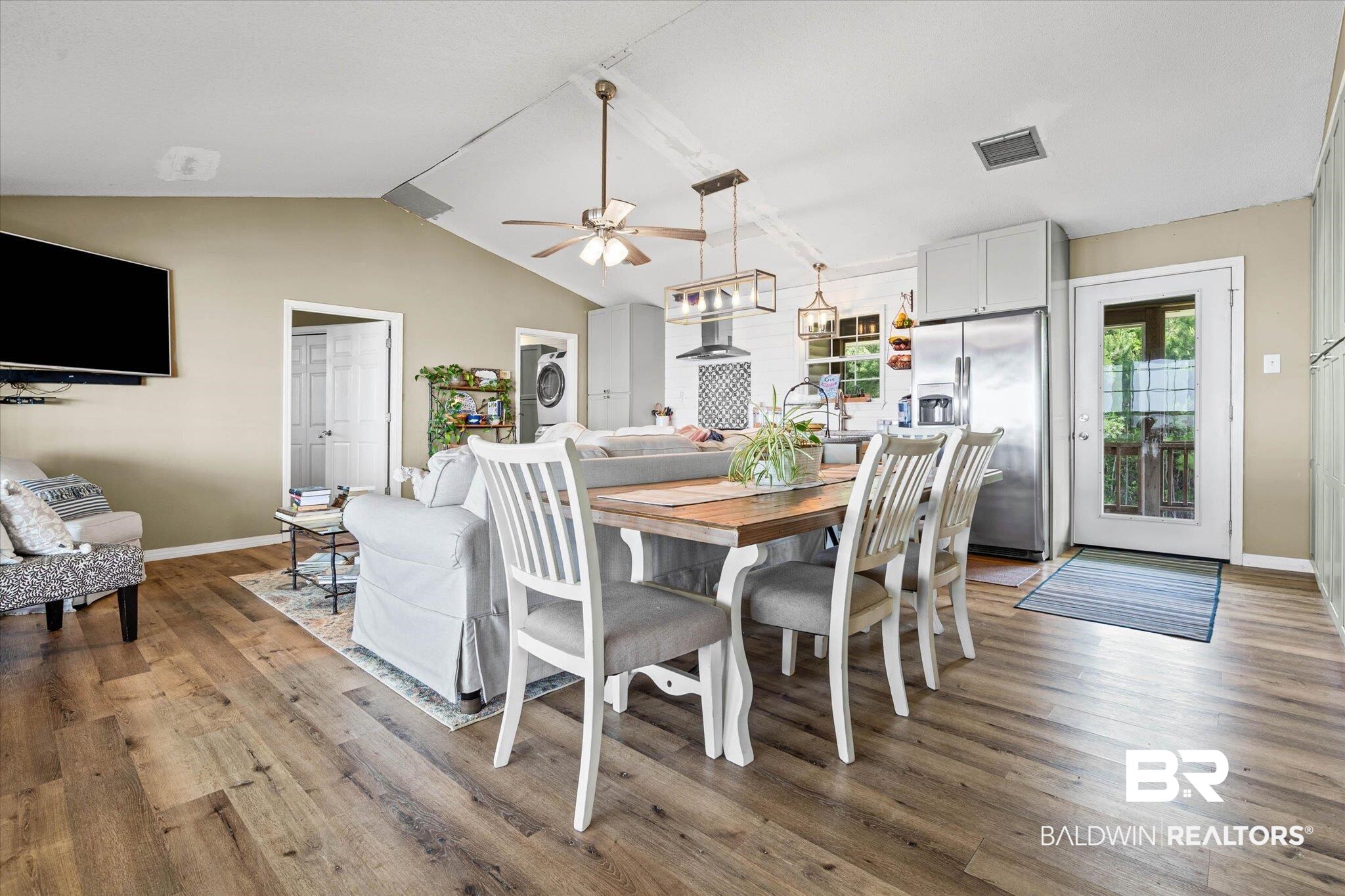 9100 Shell Belt Road Coden, AL 36523 - Photo 8 of 38 Open-concept living space featuring vaulted ceilings, wood-finish flooring, a kitchen island with pendant lighting, stainless steel refrigerator, and a glass-paneled exterior door