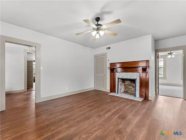 a view of an empty room with wooden floor fireplace and a window