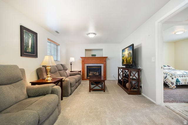 865 South 325 West Orem, UT 84058 - Photo 9 of 38 Living area featuring a fireplace with a wood mantle, light-colored carpeting, a window with blinds, and an open doorway to an additional room