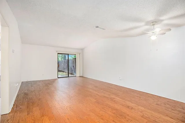 a view of an empty room with chandelier fan and wooden floor