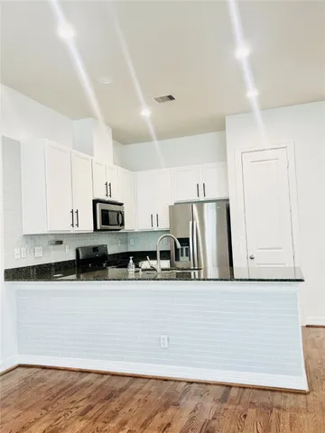 a kitchen with stainless steel appliances granite countertop a refrigerator a stove a sink and white cabinets with wooden floor