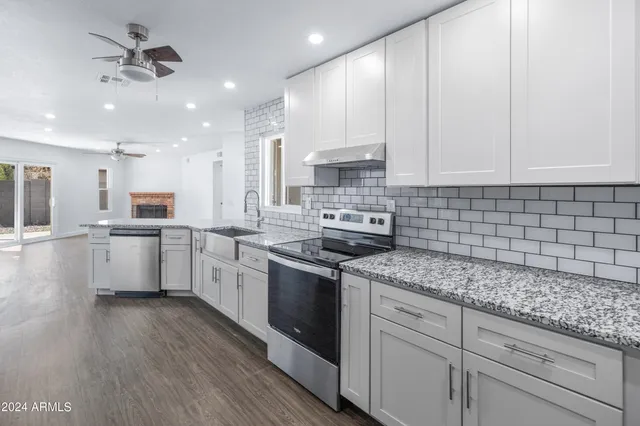 a kitchen with stainless steel appliances granite countertop a sink a stove and white cabinets with wooden floor