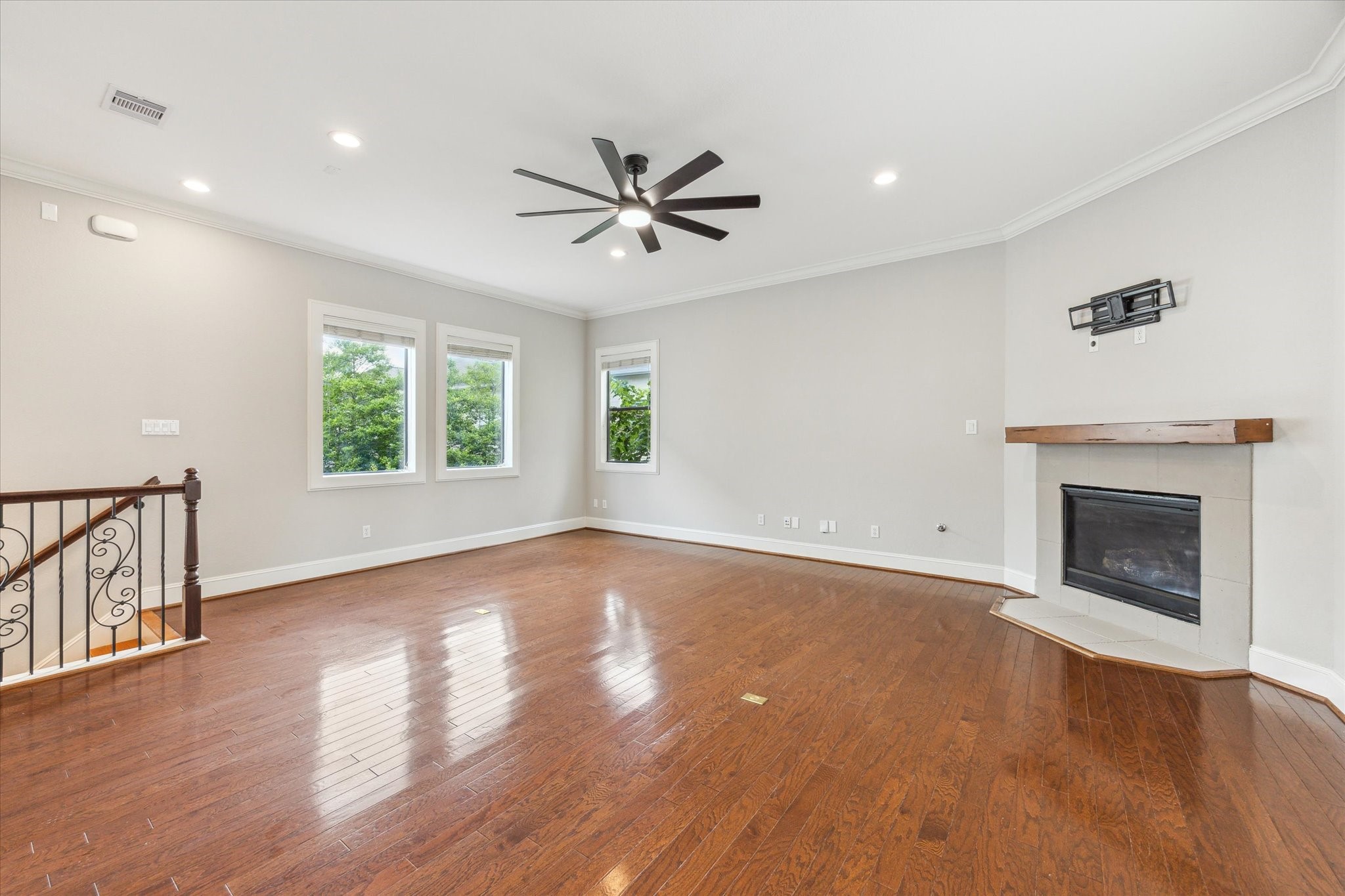 1512 Thompson Street, Unit 3 Houston, TX 77007 - Photo 3 of 32 This spacious living room features hardwood floors, a modern ceiling fan, and a corner fireplace with a wooden mantle. Large windows provide natural light, and there's a stairway with decorative railing. Ideal for cozy gatherings and relaxation.