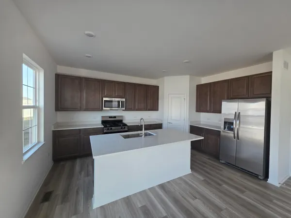 a kitchen with stainless steel appliances a sink a stove a refrigerator cabinets and a wooden floor