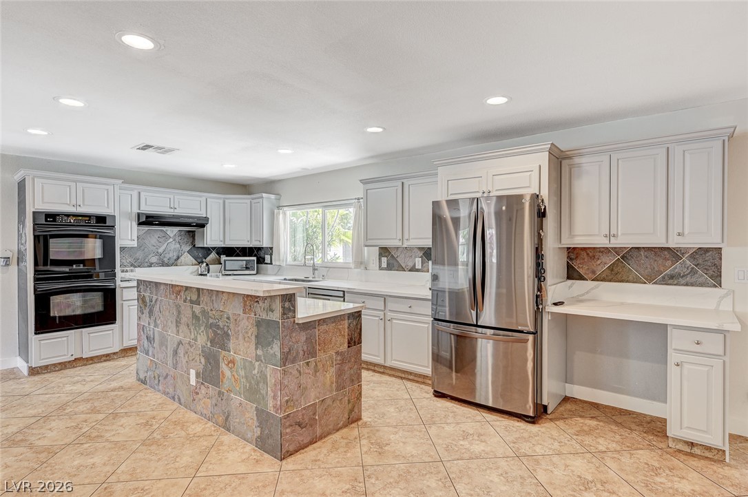 4153 Woodcrest Road Las Vegas, NV 89121 - Photo 16 of 58 Culinary adventures await in this kitchen featuring abundant white cabinetry and a striking stone-tiled island.