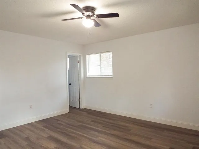 an empty room with wooden floor ceiling fan and window
