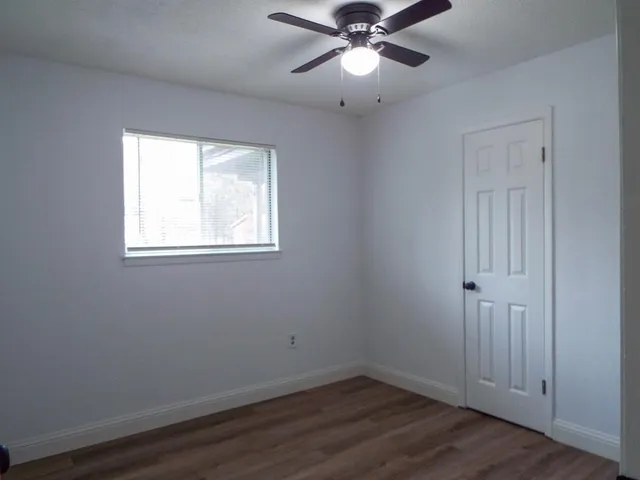 an empty room with wooden floor fan and windows