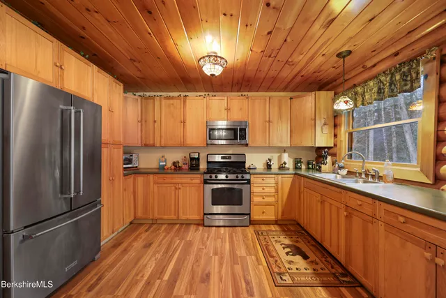 a kitchen with stainless steel appliances granite countertop a refrigerator a sink dishwasher a stove and white countertops with wooden floor