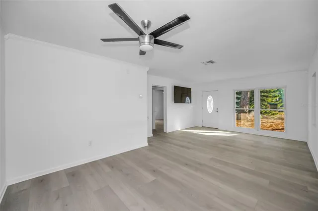 an empty room with wooden floor a ceiling fan and windows