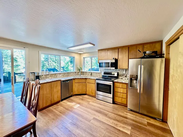a kitchen with stainless steel appliances granite countertop a refrigerator a stove top oven a sink dishwasher and wooden cabinets with wooden floor