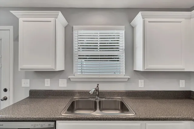 a large kitchen with granite countertop a stove a sink and white cabinets with wooden floor