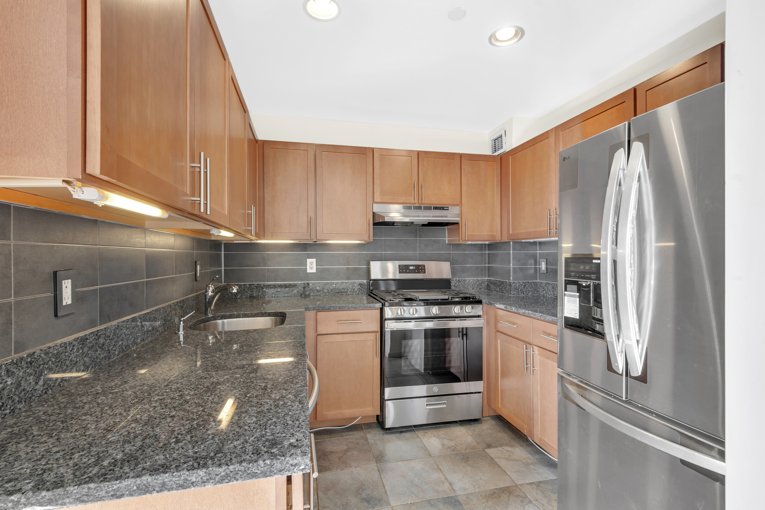 a kitchen with stainless steel appliances granite countertop a refrigerator a stove and a sink with wooden cabinets