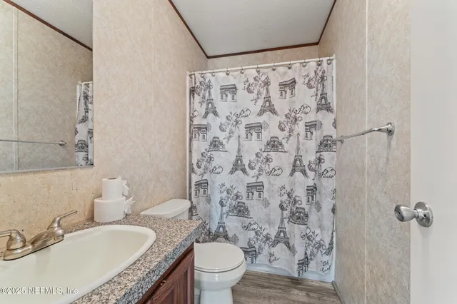 a bathroom with a granite countertop sink toilet a mirror and shower curtain