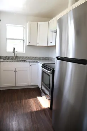 a kitchen with granite countertop a refrigerator a sink and white cabinets
