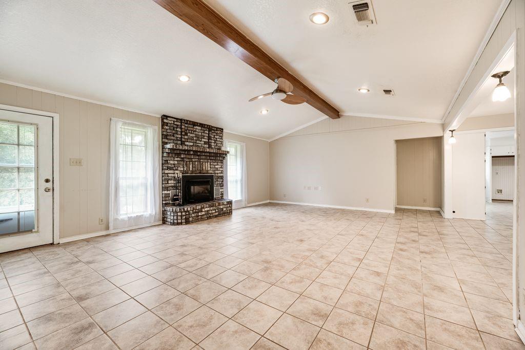 298 Butterfield Road Denison, TX 75021 - Photo 25 of 34 Spacious living area featuring a corner brick fireplace, tile flooring, and vaulted ceiling with exposed wood beam