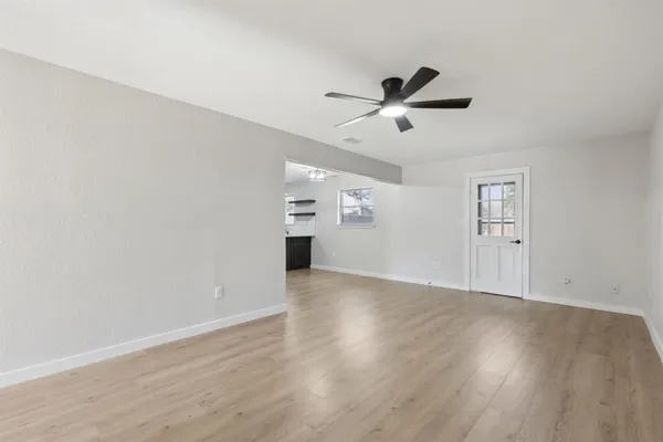an empty room with wooden floor ceiling fan and windows
