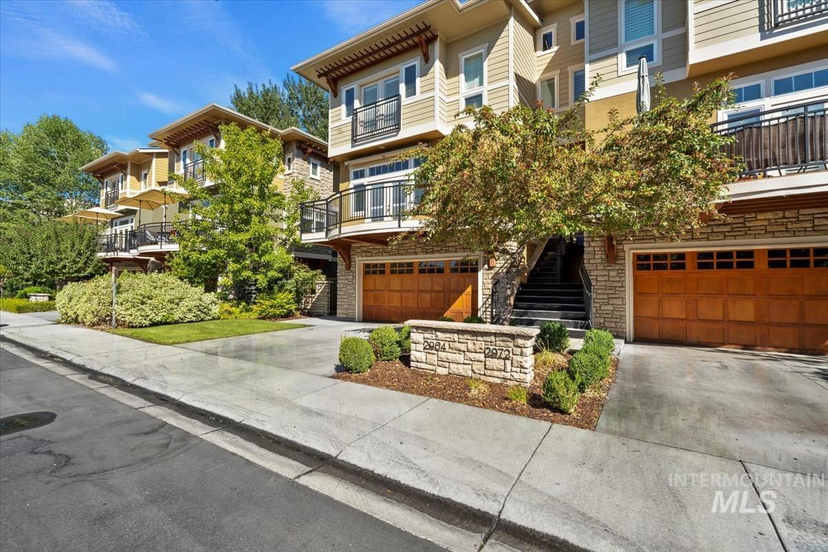 View of front facade featuring a garage, concrete driveway, stone siding, a balcony, and stairway