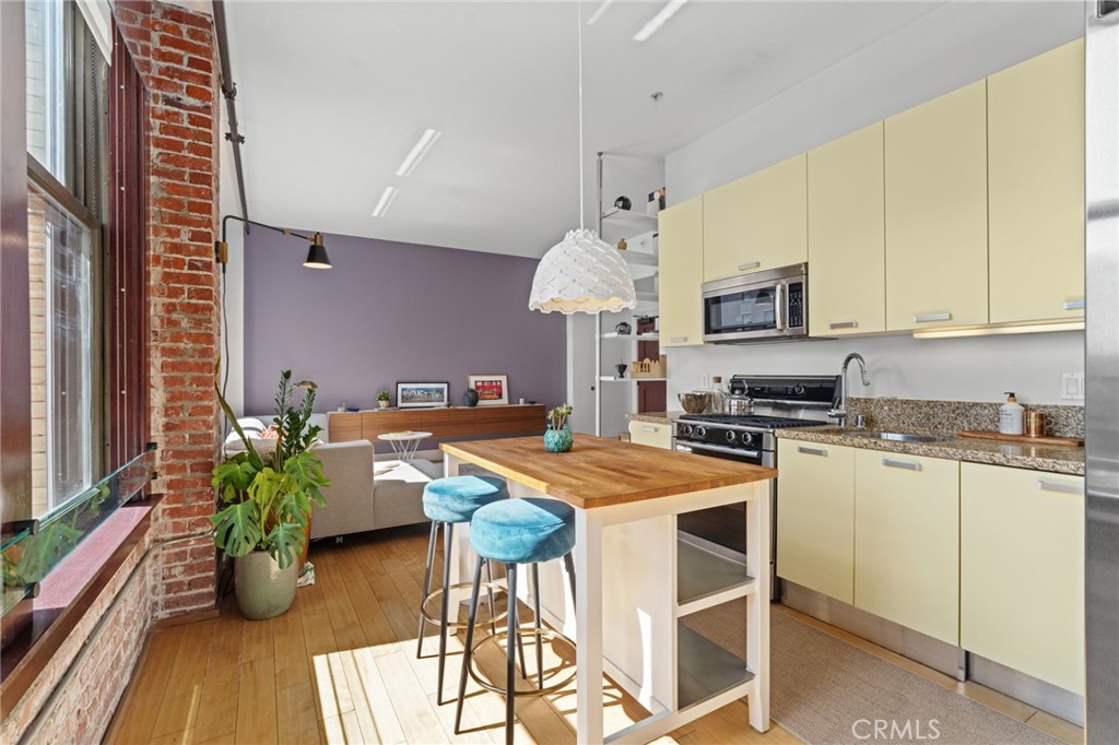 460 South Spring Street, Unit 302 Los Angeles, CA 90013 - Photo 12 of 24 a kitchen with stainless steel appliances kitchen island granite countertop a stove a sink dishwasher and white cabinets with wooden floor