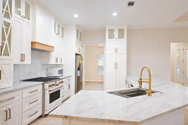 a kitchen with stainless steel appliances granite countertop a stove top oven a sink a refrigerator and white cabinets