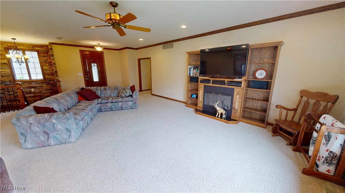 10323 Smith Road Litchfield, OH 44253 - Photo 8 of 50 Living area featuring visible vents, baseboards, ornamental molding, ceiling fan with notable chandelier, and a glass covered fireplace