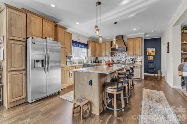 a kitchen with stainless steel appliances kitchen island granite countertop a refrigerator a stove a sink a dining table and chairs with wooden floor