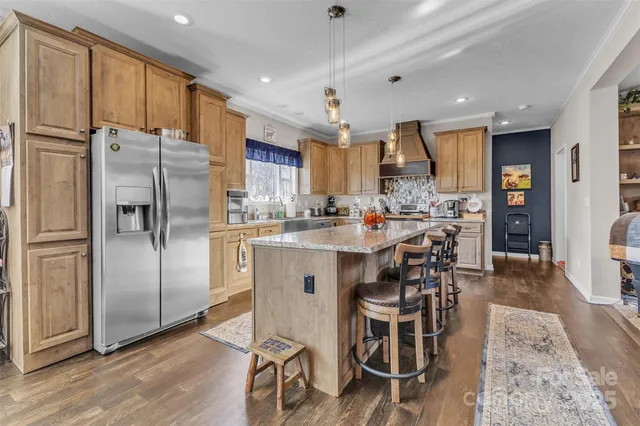 a kitchen with stainless steel appliances kitchen island granite countertop a refrigerator a stove a sink a dining table and chairs with wooden floor
