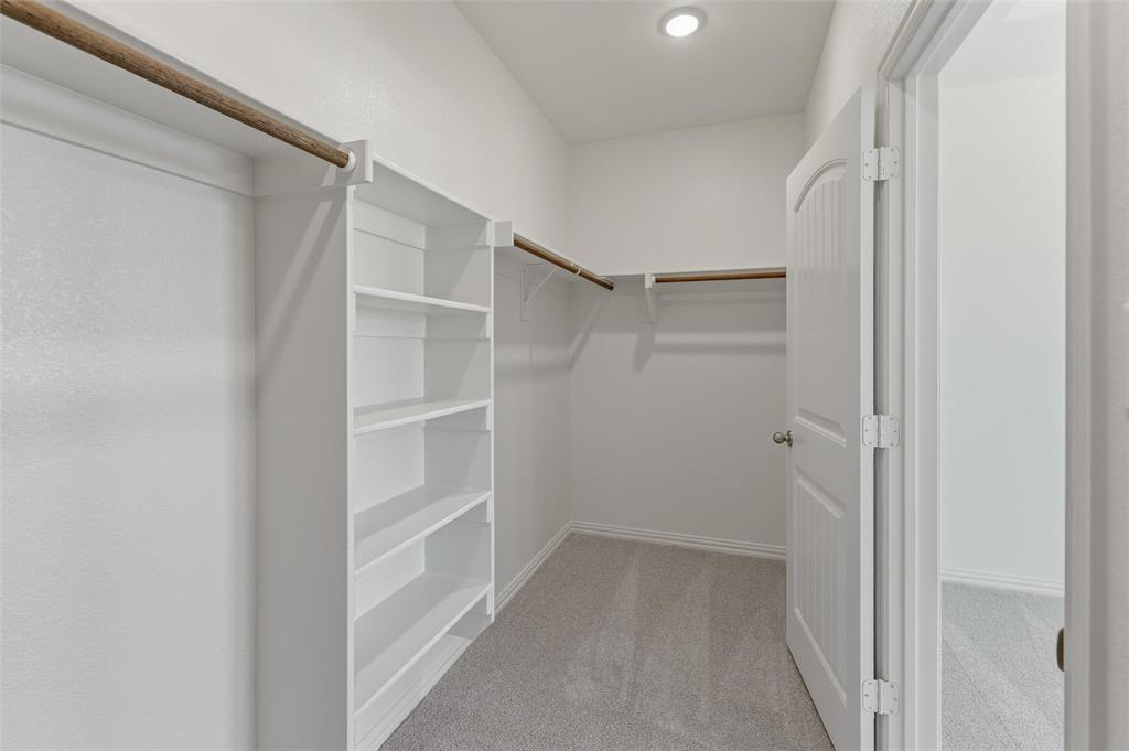 130 Fossil Canyon Drive Rhome, TX 76078 - Photo 17 of 25 Spacious walk-in closet featuring built-in shelving, dual hanging rods, light gray carpeting, a recessed ceiling light, and a paneled interior door