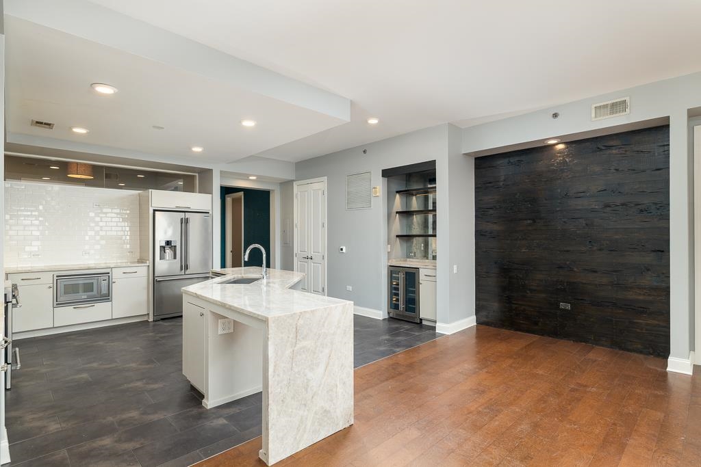 717 Riverside Drive, Unit 1105 Memphis, TN 38103 - Photo 7 of 29 Kitchen featuring a center island with sink, light stone countertops, white cabinetry, beverage cooler, and high quality fridge