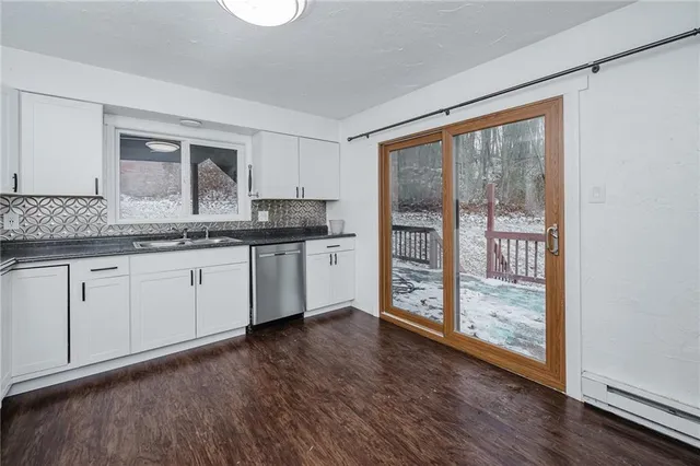 a kitchen with stainless steel appliances granite countertop a stove a sink and white cabinets with wooden floor next to windows