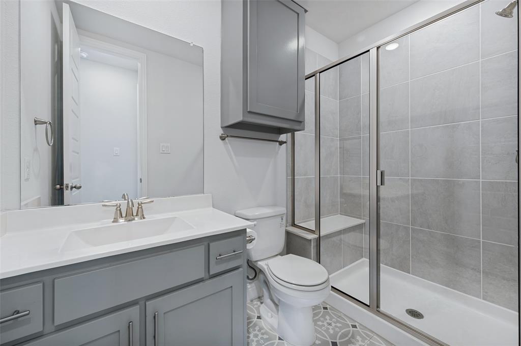 15862 Shasta Daisy Road Frisco, TX 75035 - Photo 9 of 15 Downstairs full bath with step in shower, vanity with light-toned countertop, integrated rectangular sink, gray cabinetry, and decorator tile flooring.