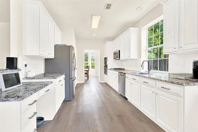 a large kitchen with stainless steel appliances granite countertop a stove a sink dishwasher a refrigerator white cabinets and wooden floor next to a window