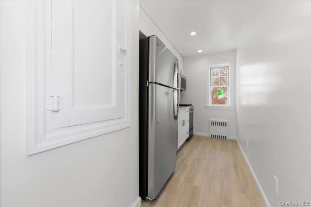 a view of hallway with stainless steel appliances wooden floor and more cabinets