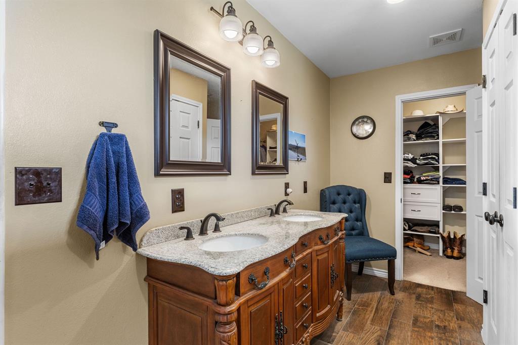13315 Highway 281 Scotland, TX 76379 - Photo 18 of 40 Bathroom featuring a dual vanity with a granite-style countertop, wood-finish flooring, framed mirrors, and an organized walk-in closet