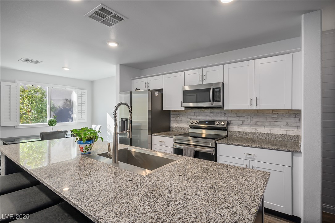 12236 Glass Desert Road, Unit 2 Las Vegas, NV 89183 - Photo 11 of 32 Kitchen featuring stainless steel appliances, a kitchen breakfast bar, light stone countertops, and recessed lighting