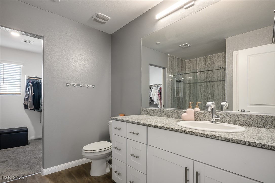 12236 Glass Desert Road, Unit 2 Las Vegas, NV 89183 - Photo 25 of 32 Bathroom featuring a walk in closet, vanity, a stall shower, and dark wood-type flooring