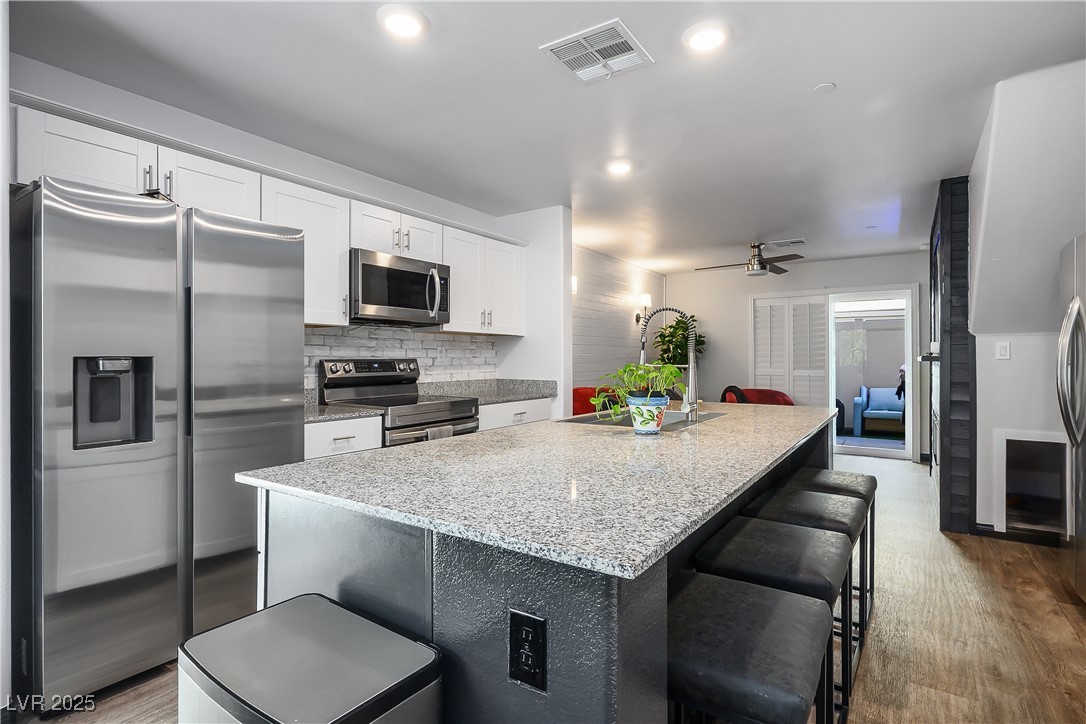 12236 Glass Desert Road, Unit 2 Las Vegas, NV 89183 - Photo 9 of 32 Kitchen with appliances with stainless steel finishes, a breakfast bar, light stone countertops, backsplash, and a kitchen island