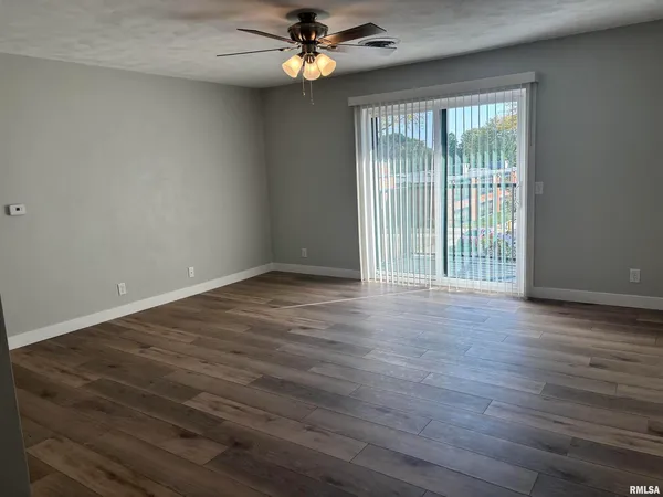 an empty room with wooden floor fan and windows
