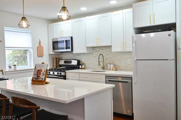 a kitchen with stainless steel appliances a sink a stove a refrigerator a center island and cabinets