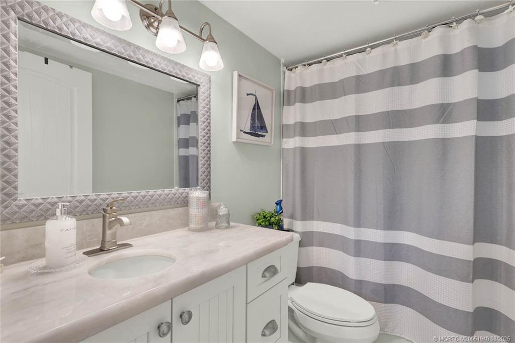 1950 Southwest Palm City Road, Unit 9108 Stuart, FL 34994 - Photo 29 of 37 a bathroom with a granite countertop sink a toilet a mirror and shower curtain