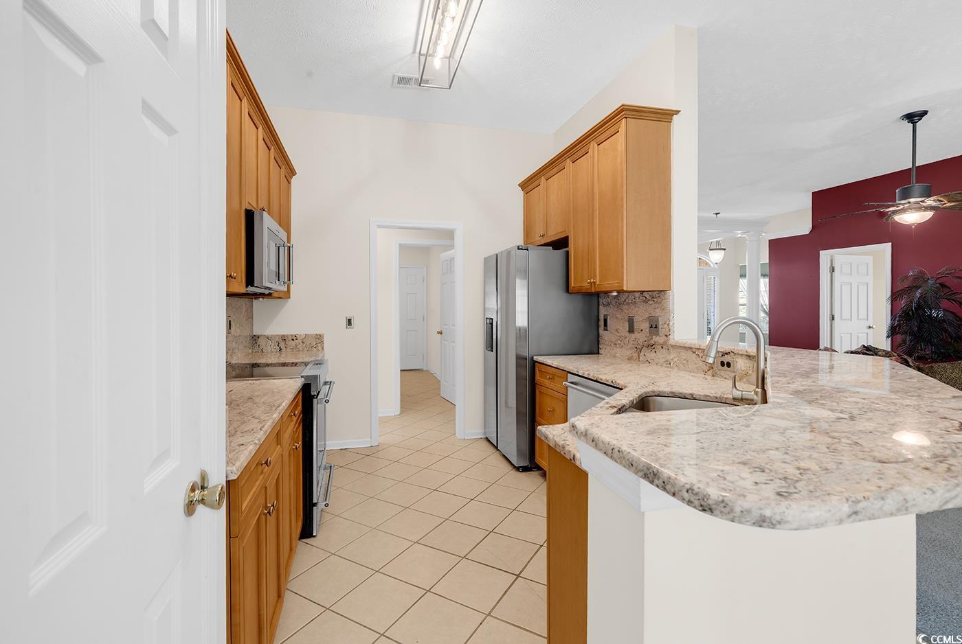 246 Catawba River Road Myrtle Beach, SC 29588 - Photo 16 of 27 Kitchen with a peninsula, stainless steel appliances, light tile patterned flooring, tasteful backsplash, and light stone countertops