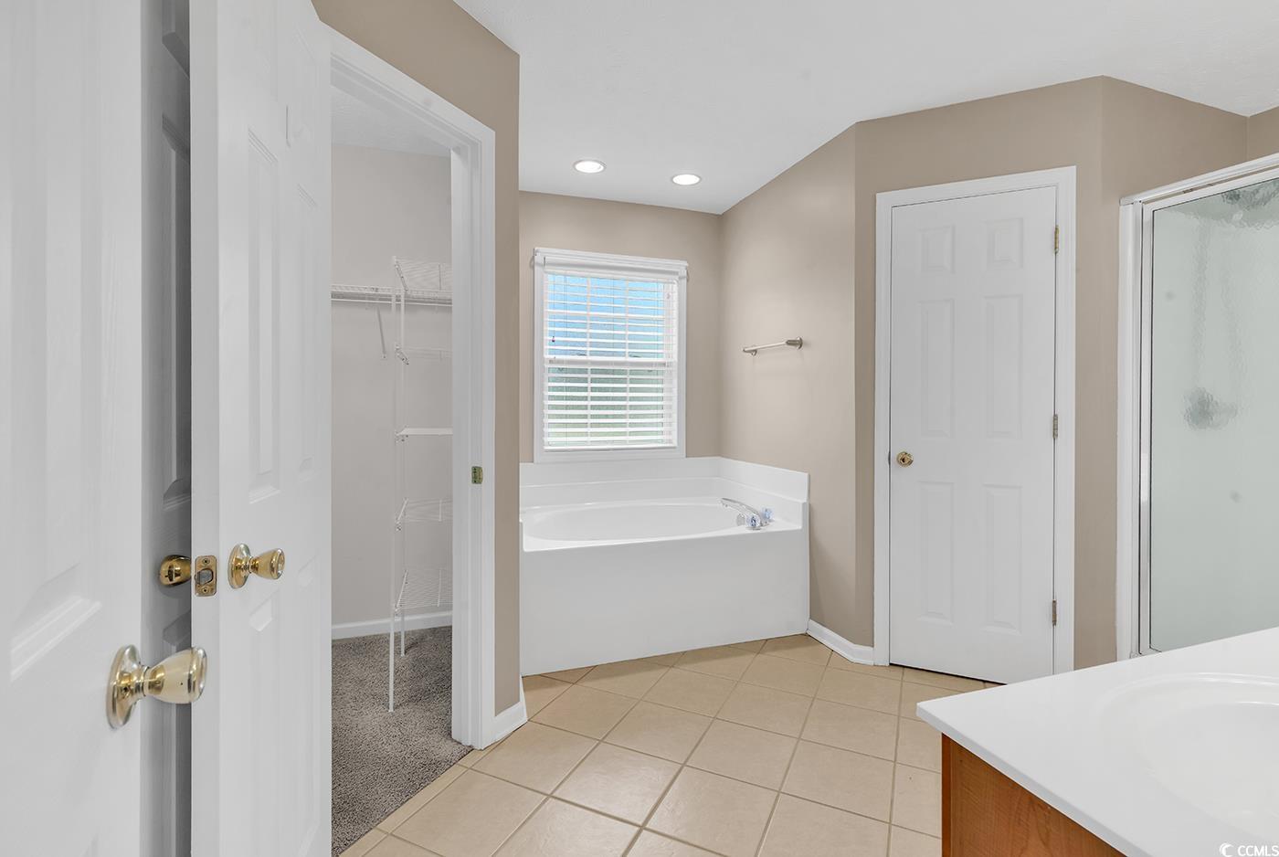 Bathroom featuring light tile patterned floors, a bath, a spacious closet, vanity, and a shower stall